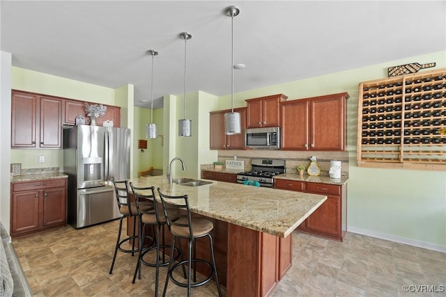 kitchen featuring stainless steel appliances, hanging light fixtures, an island with sink, light stone countertops, and a kitchen bar