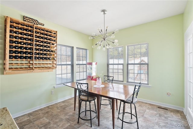 dining space featuring a chandelier, stone finish floor, a healthy amount of sunlight, and baseboards