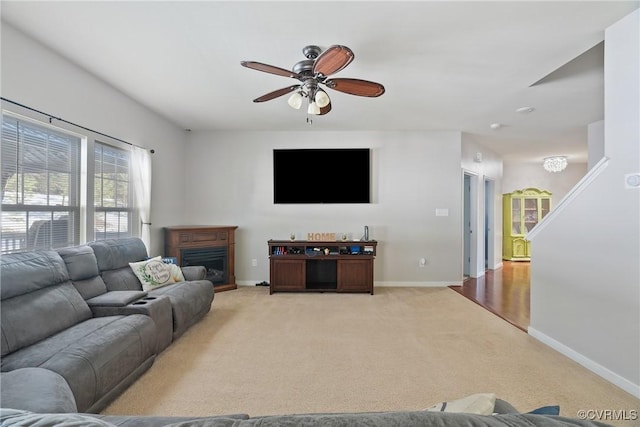 living area with baseboards, ceiling fan, a glass covered fireplace, and light colored carpet