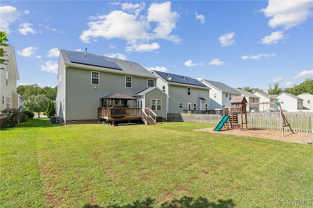 rear view of property featuring a playground, a yard, roof mounted solar panels, crawl space, and a residential view