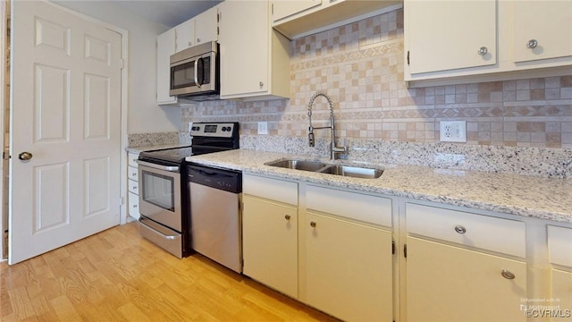 kitchen with decorative backsplash, light stone counters, stainless steel appliances, sink, and light hardwood / wood-style flooring