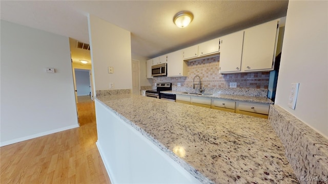 kitchen with backsplash, sink, light hardwood / wood-style flooring, light stone countertops, and stainless steel appliances