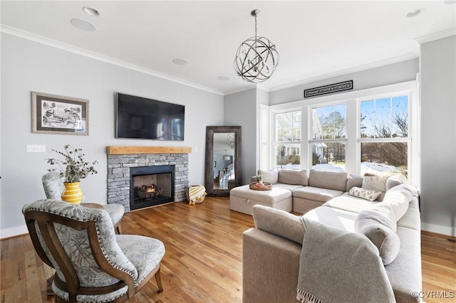 living room featuring ornamental molding, light hardwood / wood-style flooring, a stone fireplace, and a notable chandelier