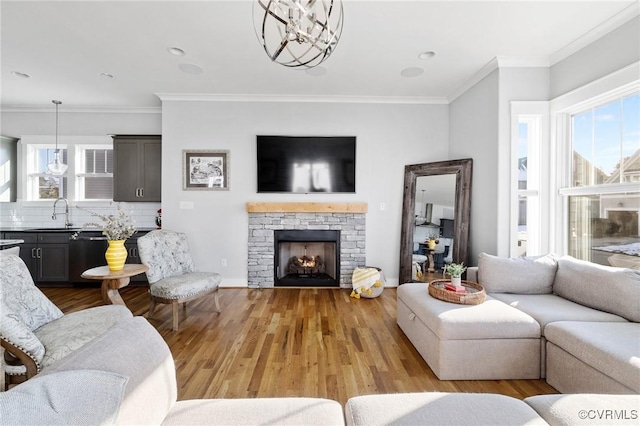 living room featuring light wood-type flooring, an inviting chandelier, a stone fireplace, and ornamental molding