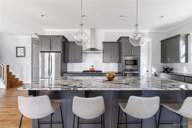 kitchen featuring stainless steel appliances, wall chimney exhaust hood, a kitchen bar, and pendant lighting