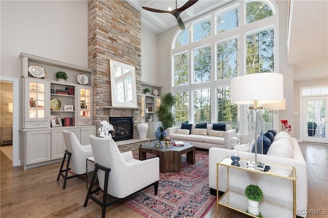 living room with hardwood / wood-style flooring, ceiling fan, a stone fireplace, and a towering ceiling