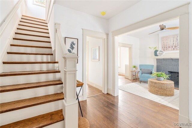 stairs featuring ceiling fan, a fireplace, and wood-type flooring