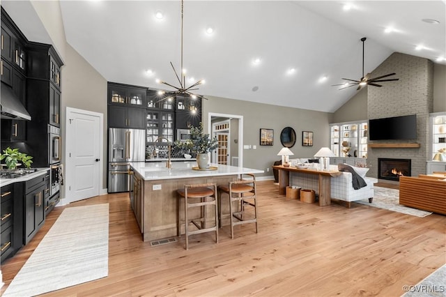 kitchen with a large island, a stone fireplace, stainless steel fridge with ice dispenser, high vaulted ceiling, and light wood-type flooring