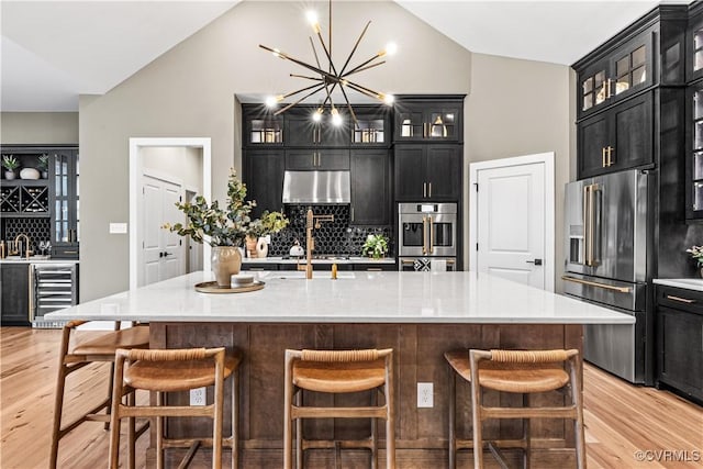 kitchen with a kitchen breakfast bar, backsplash, lofted ceiling, a kitchen island with sink, and appliances with stainless steel finishes