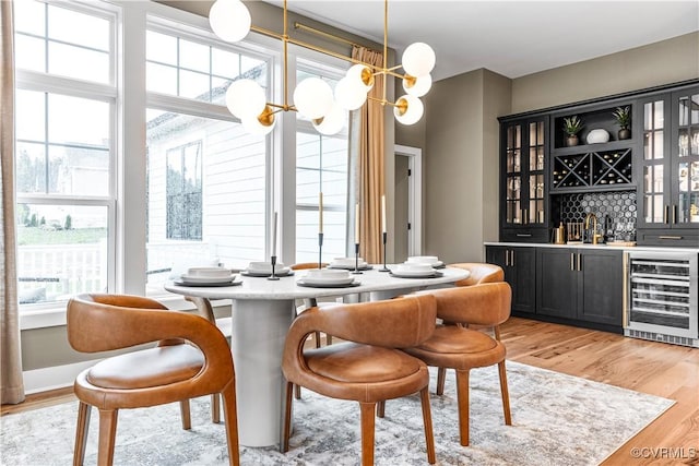 dining room with light hardwood / wood-style floors, beverage cooler, a notable chandelier, and indoor wet bar