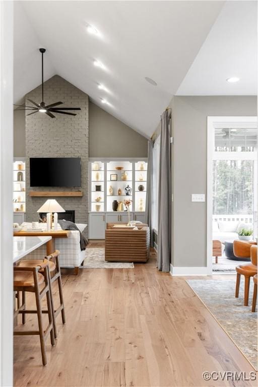 interior space with ceiling fan, light wood-type flooring, vaulted ceiling, and a brick fireplace