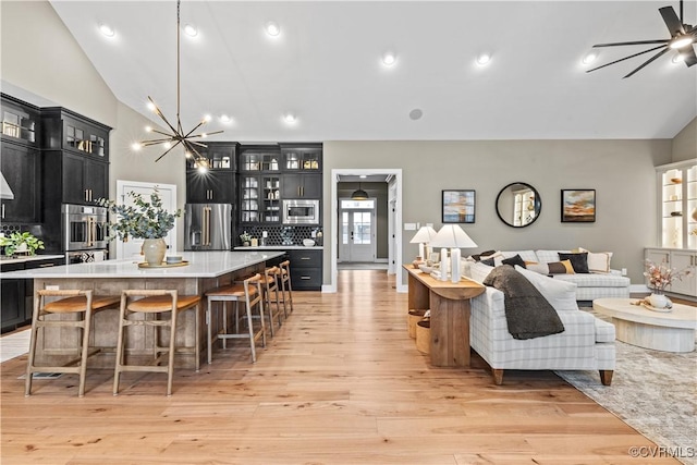 kitchen featuring a large island, light hardwood / wood-style floors, lofted ceiling, decorative backsplash, and appliances with stainless steel finishes