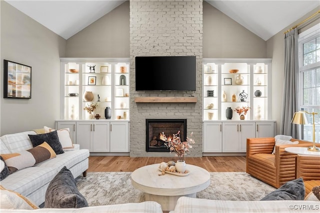 living room featuring light wood-type flooring, vaulted ceiling, and a brick fireplace