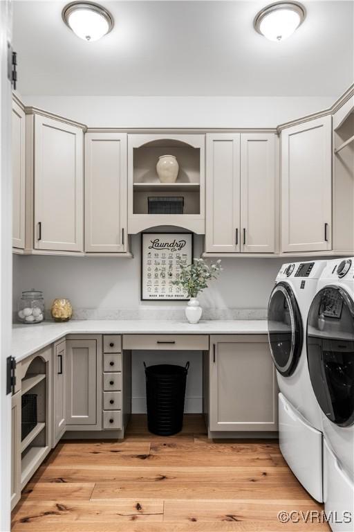 clothes washing area with cabinets, light hardwood / wood-style flooring, and washing machine and clothes dryer