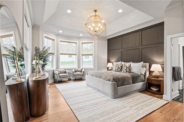 bedroom featuring a raised ceiling, ornamental molding, light wood-type flooring, and an inviting chandelier