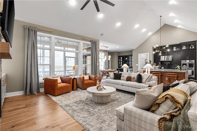 living room featuring ceiling fan with notable chandelier, light wood-type flooring, high vaulted ceiling, and a healthy amount of sunlight