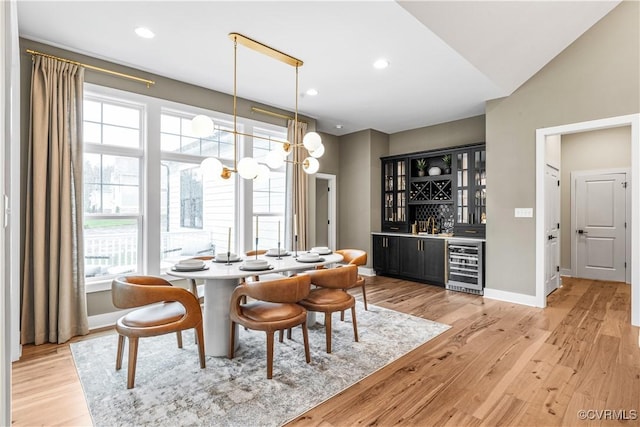 dining room featuring beverage cooler, light wood-type flooring, bar, and vaulted ceiling