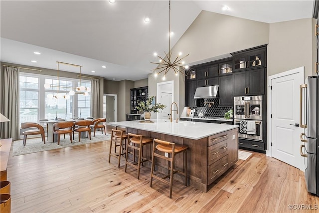 kitchen featuring pendant lighting, backsplash, an inviting chandelier, an island with sink, and appliances with stainless steel finishes