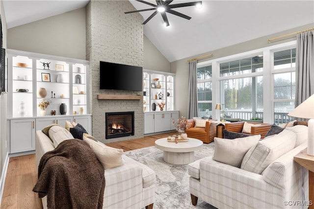 living room featuring ceiling fan, high vaulted ceiling, light wood-type flooring, and a brick fireplace