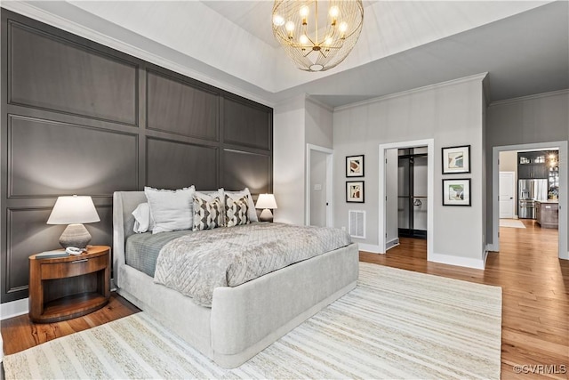 bedroom featuring connected bathroom, crown molding, light hardwood / wood-style flooring, and a chandelier