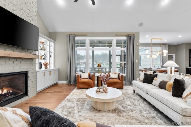 living room featuring a fireplace, vaulted ceiling, light hardwood / wood-style flooring, and ceiling fan with notable chandelier