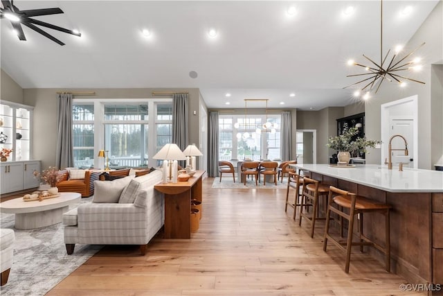 living room featuring ceiling fan with notable chandelier, light hardwood / wood-style floors, sink, and vaulted ceiling