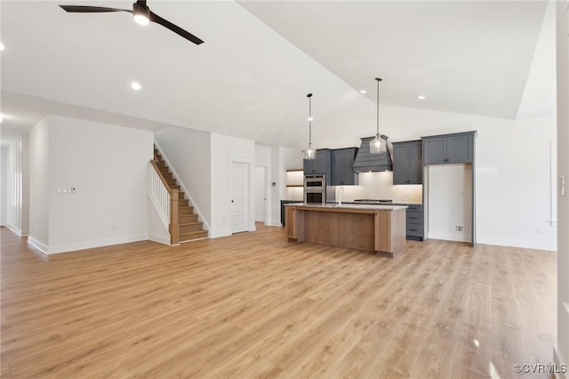 kitchen with light hardwood / wood-style floors, a center island with sink, ceiling fan, decorative backsplash, and decorative light fixtures