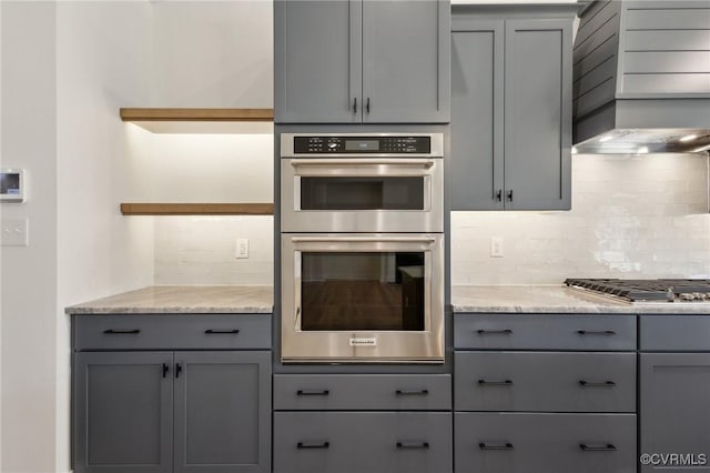 kitchen featuring light stone countertops, stainless steel appliances, wall chimney range hood, and gray cabinets