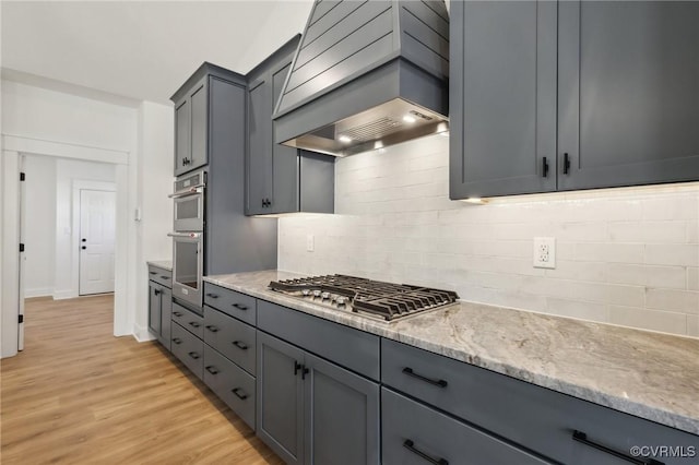 kitchen featuring light hardwood / wood-style floors, stainless steel appliances, tasteful backsplash, custom range hood, and light stone countertops