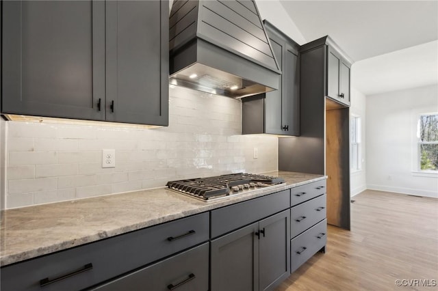 kitchen featuring light stone countertops, premium range hood, gray cabinets, light wood-type flooring, and stainless steel gas stovetop