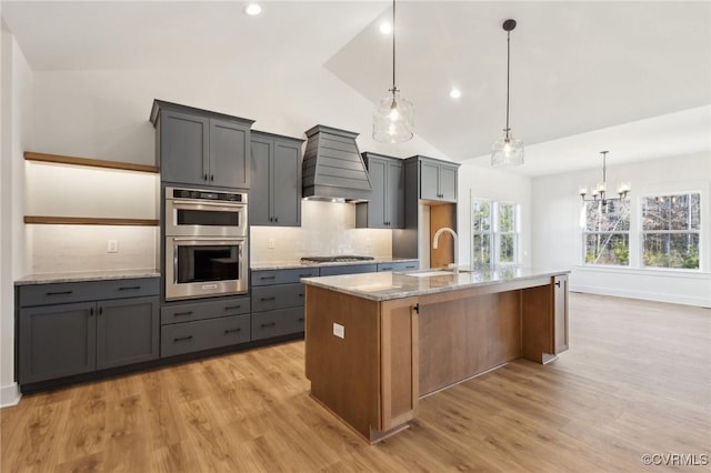 kitchen featuring appliances with stainless steel finishes, a center island with sink, light stone counters, and custom range hood