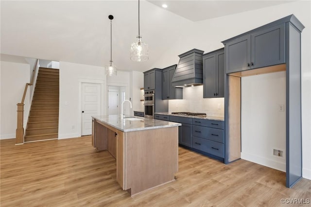 kitchen featuring vaulted ceiling, custom exhaust hood, hanging light fixtures, light stone countertops, and an island with sink