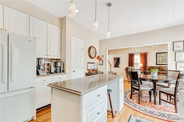 kitchen with light stone counters, pendant lighting, white refrigerator, a center island, and white cabinetry