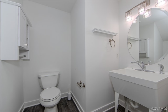 half bath with toilet, a sink, baseboards, and wood finished floors