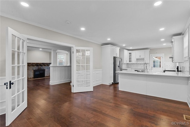 kitchen with a stone fireplace, kitchen peninsula, french doors, stainless steel refrigerator with ice dispenser, and white cabinets