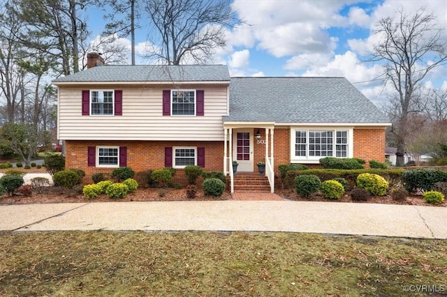 tri-level home featuring brick siding, roof with shingles, and a chimney