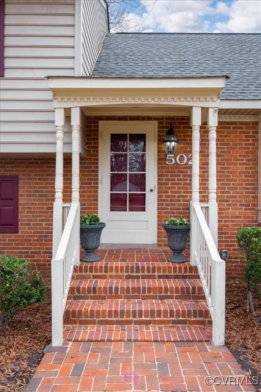 property entrance featuring brick siding and roof with shingles