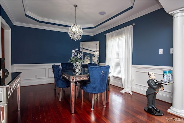 dining area featuring a raised ceiling, crown molding, dark wood-type flooring, an inviting chandelier, and decorative columns