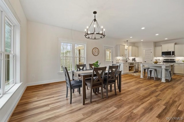 dining space with sink, a notable chandelier, and light wood-type flooring