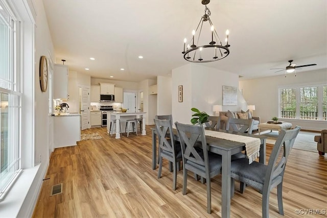 dining room with ceiling fan with notable chandelier and light hardwood / wood-style flooring