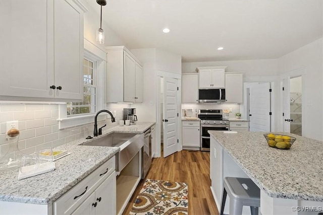 kitchen featuring white cabinets, appliances with stainless steel finishes, light hardwood / wood-style flooring, and light stone countertops