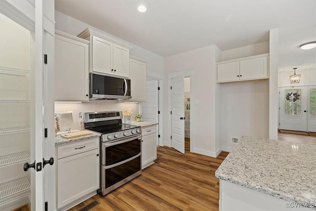 kitchen with light stone countertops, backsplash, appliances with stainless steel finishes, white cabinets, and light wood-type flooring