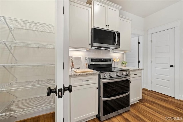 kitchen featuring light stone countertops, stainless steel appliances, wood-type flooring, decorative backsplash, and white cabinets