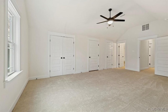 unfurnished bedroom featuring two closets, ceiling fan, light carpet, and lofted ceiling