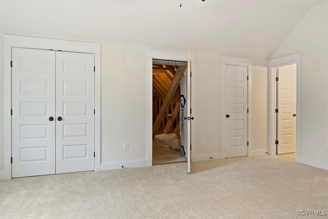 unfurnished bedroom with light colored carpet, multiple closets, and lofted ceiling