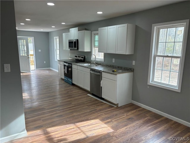 kitchen with white cabinets, dark hardwood / wood-style flooring, appliances with stainless steel finishes, and dark stone counters