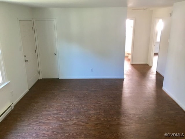 empty room featuring a healthy amount of sunlight, dark hardwood / wood-style flooring, and a baseboard heating unit