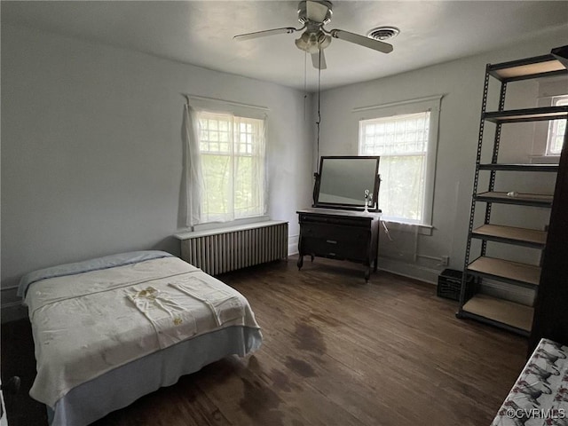 bedroom with ceiling fan, radiator heating unit, dark hardwood / wood-style floors, and multiple windows