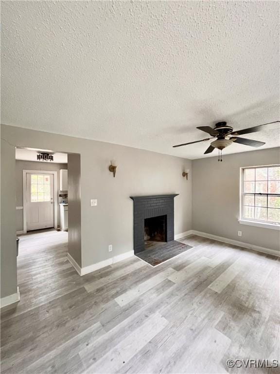 unfurnished living room with ceiling fan, light wood-type flooring, a textured ceiling, and a brick fireplace