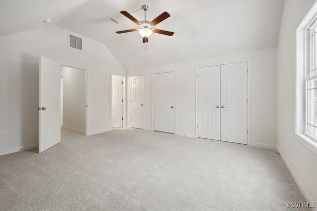 unfurnished bedroom with multiple closets, lofted ceiling, visible vents, light colored carpet, and baseboards